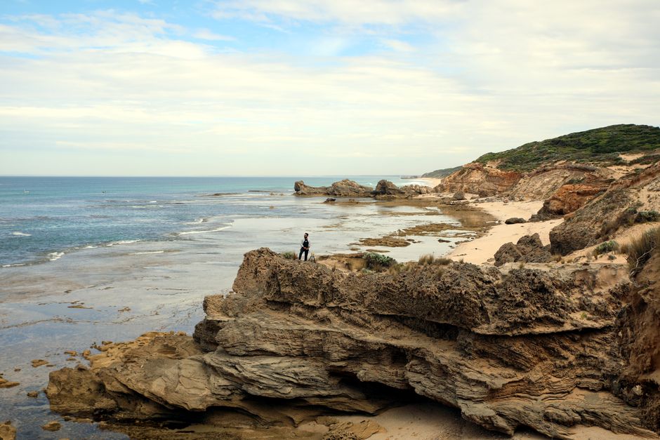 A solitary person stands on a rocky cliff overlooking the ocean, capturing the vast and serene coastal landscape.