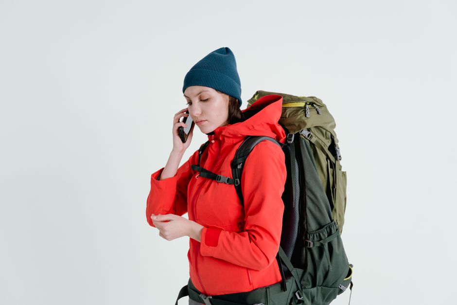 Woman in red jacket with backpack taking a phone call, ready for adventure.
