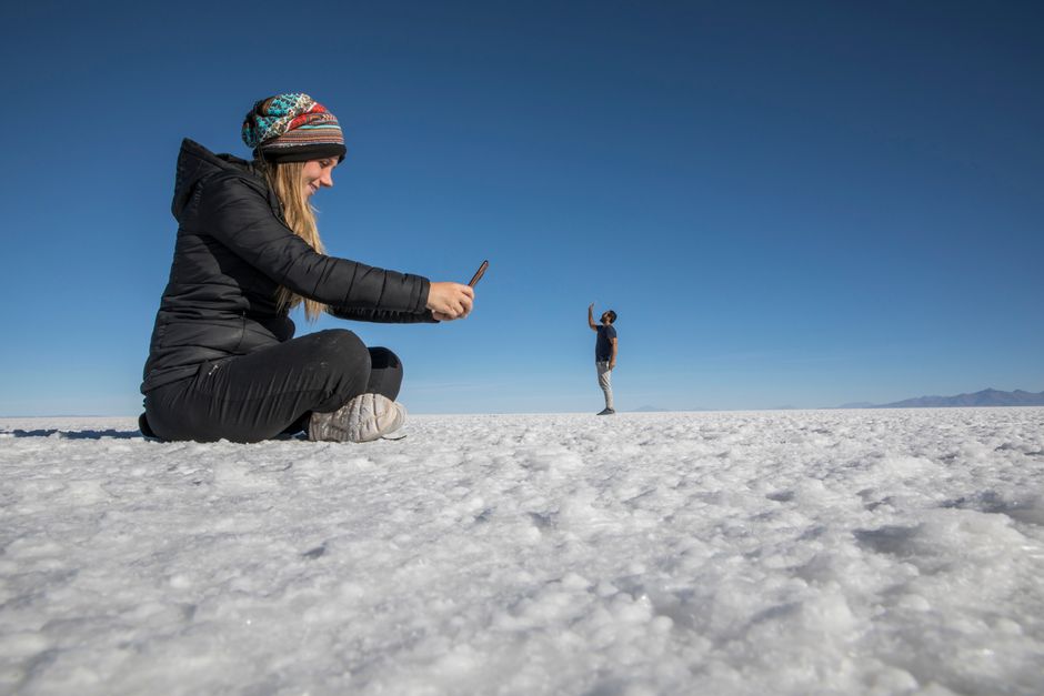 A woman takes a creative perspective photo of a man at the expansive Uyuni Salt Flats in Bolivia.