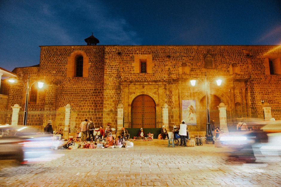 A vibrant evening outside a historic church in Cusco, Peru, with street life and motion blur.