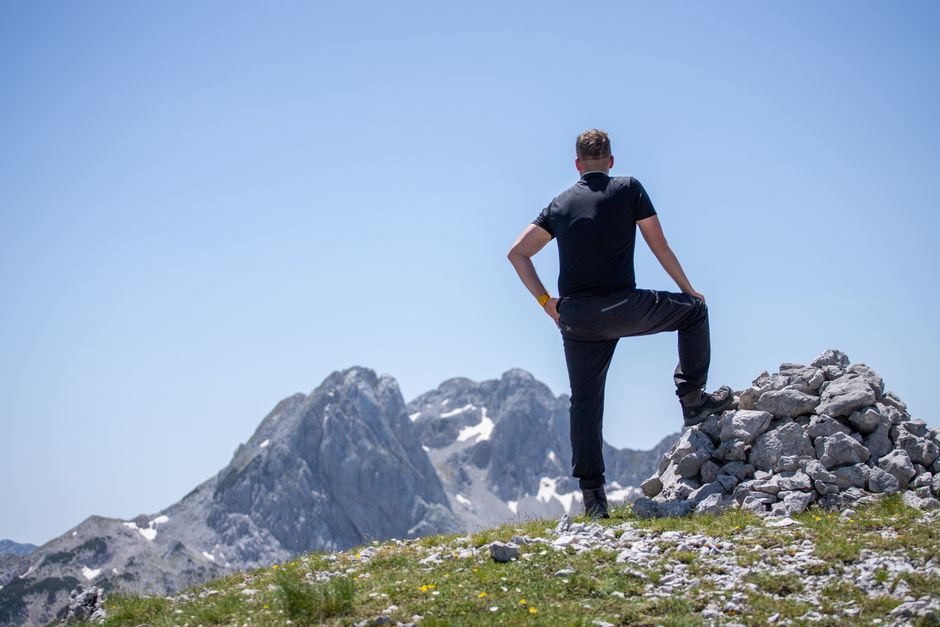 A hiker stands atop a rocky peak, enjoying a breathtaking mountain view on a clear day.