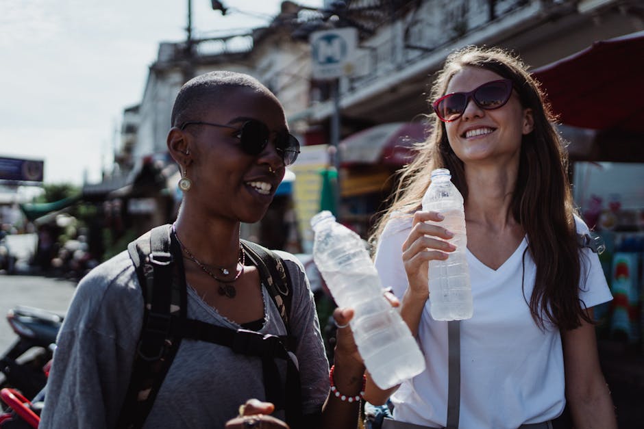 Two young women enjoying a city adventure, holding water bottles, and smiling under the summer sun.