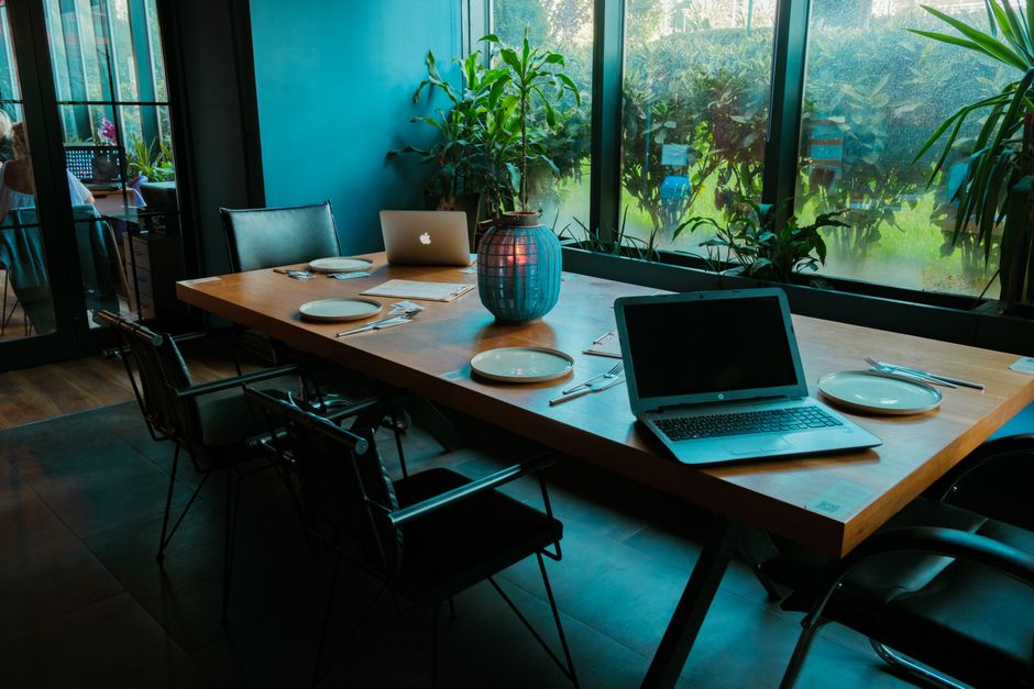 Cozy dining area with laptops, chairs, and decor against a window view.