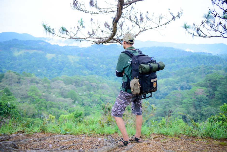 A man with a backpack stands on a cliff, admiring scenic mountain views.