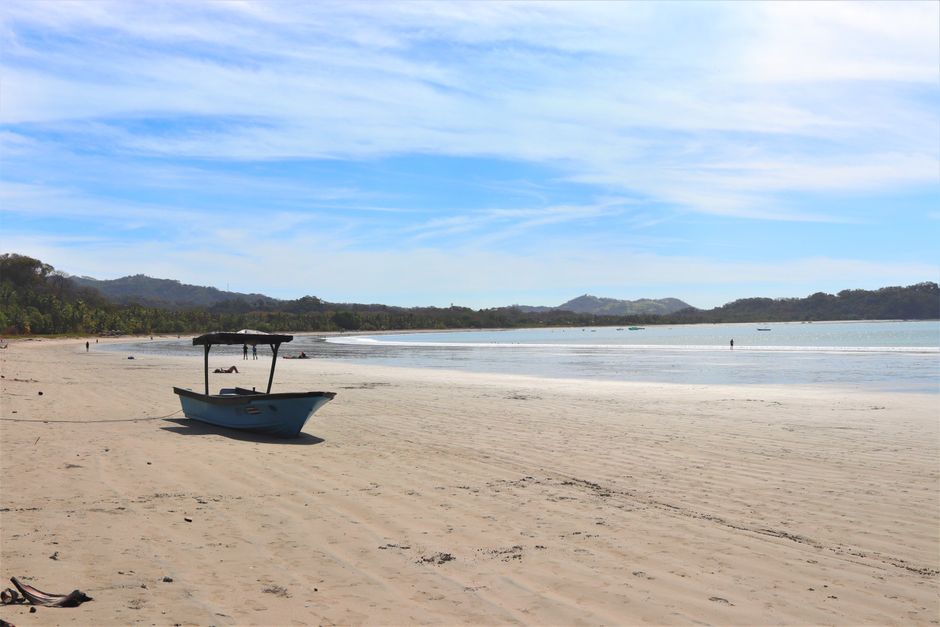 Tranquil beach scene at Sámara, Costa Rica, featuring a lone boat on sandy shores under a blue sky.