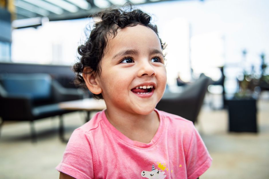 Cheerful young girl with curly hair smiling brightly in an indoor setting, exuding happiness.