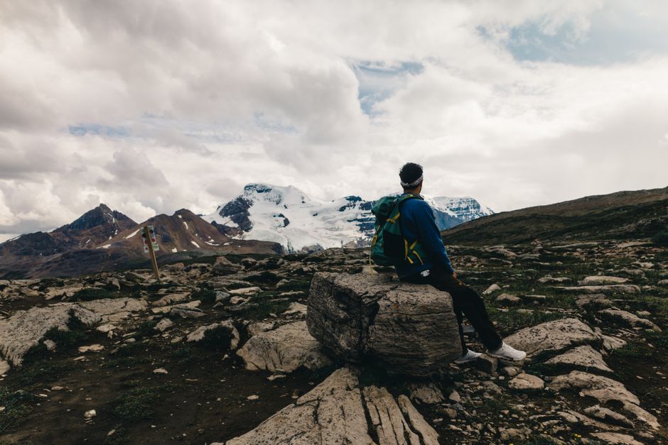 A hiker sits on a rock admiring the stunning mountain landscape in Jasper, Alberta, Canada.