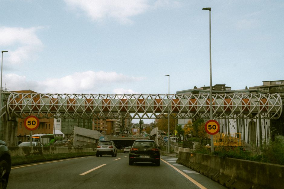 City highway with a distinctive lattice-patterned overpass and traffic, 50 km/h speed limit signs in view.