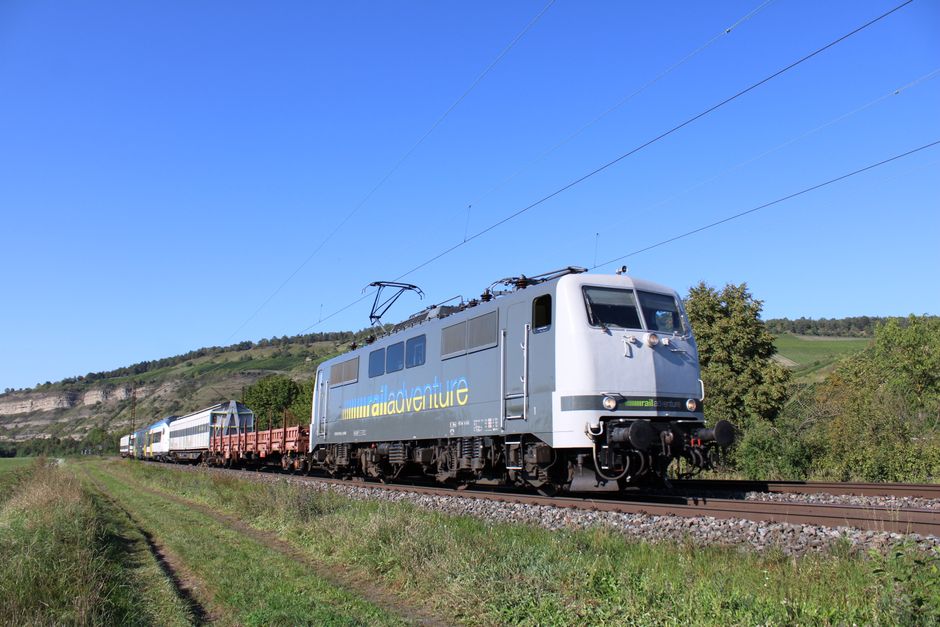 A sleek cargo train travels through a rural landscape under a clear blue sky.
