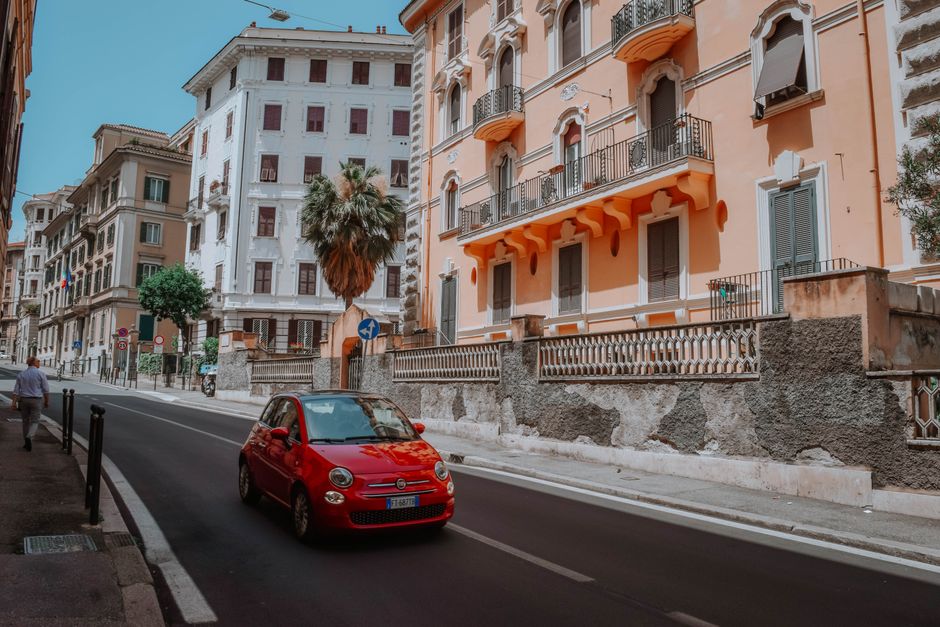 A scenic urban street in Rome showcasing classic Italian architecture with a red car adding vibrant contrast.