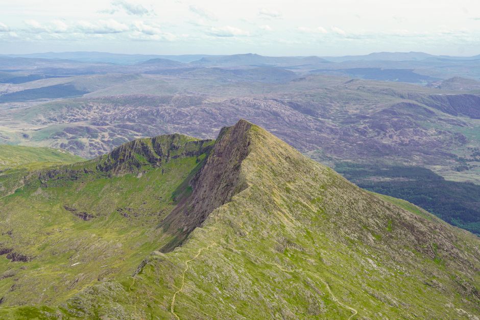 Breathtaking aerial view of a rugged green mountain summit with expansive valley in the background.