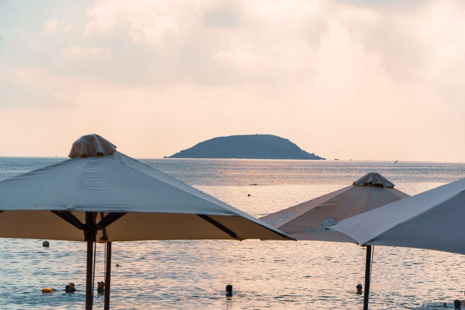 Serene beach scene with umbrellas and swimmers at sunset, overlooking a distant island.