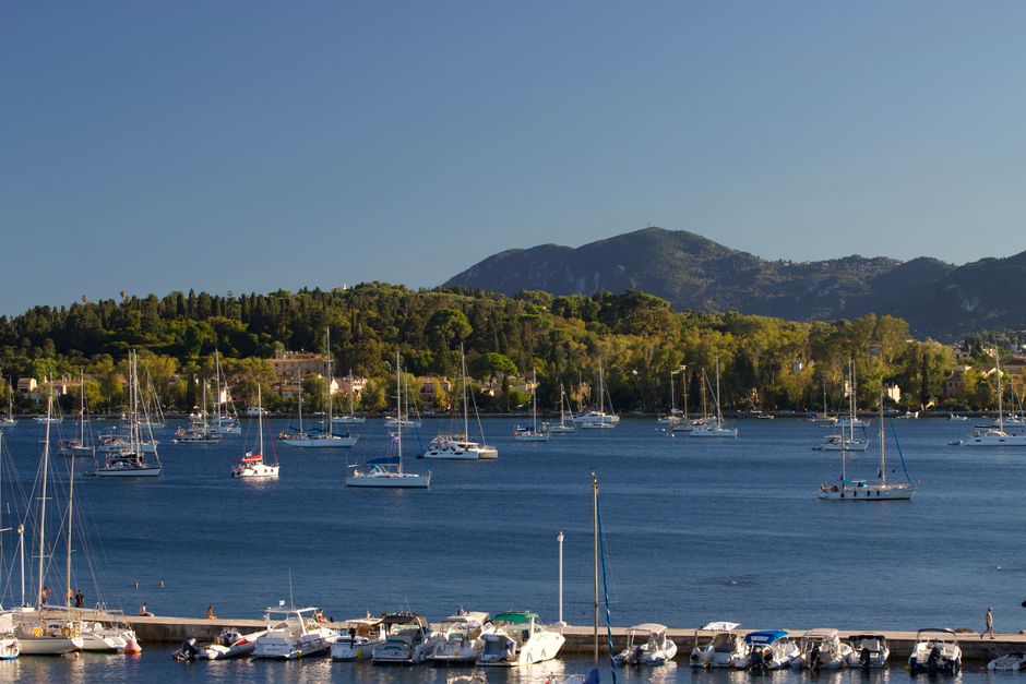 Beautiful panoramic view of boats in the harbor with green hills in Corfu, Greece during summer.