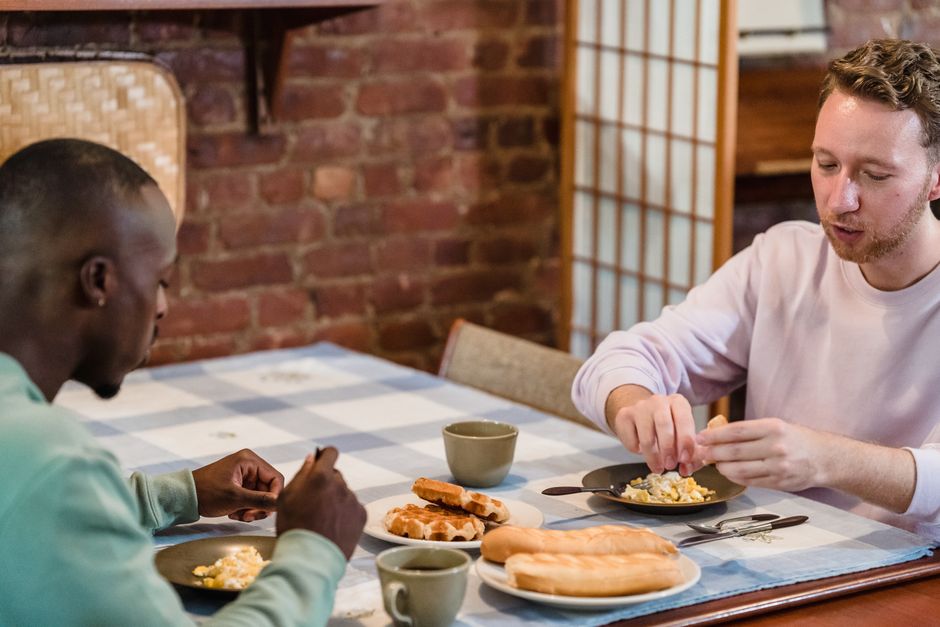 Two men having a casual breakfast with eggs and baguette in a cosy kitchen setting.