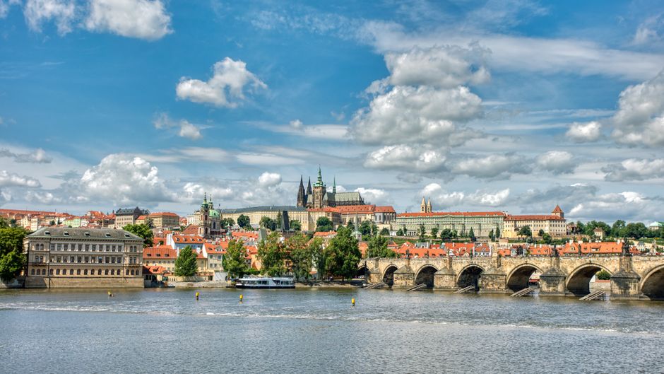 A vibrant cityscape of Prague featuring the iconic Charles Bridge and Prague Castle under a blue sky.