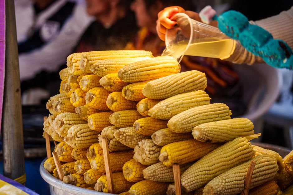 A vendor pouring sauce over grilled corn at a market in Ciudad de Guatemala.
