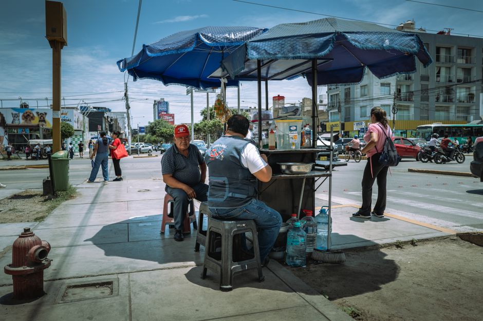 A bustling street food stand in Trujillo, Peru under a blue canopy on a sunny day.