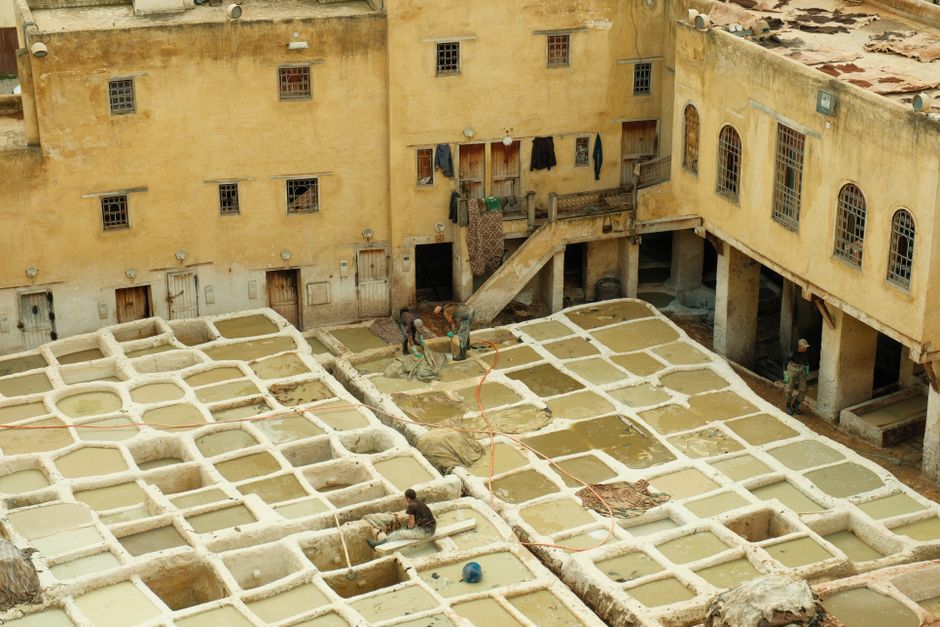Aerial view of a traditional leather tannery in Fes, Morocco, with workers and dye vats.