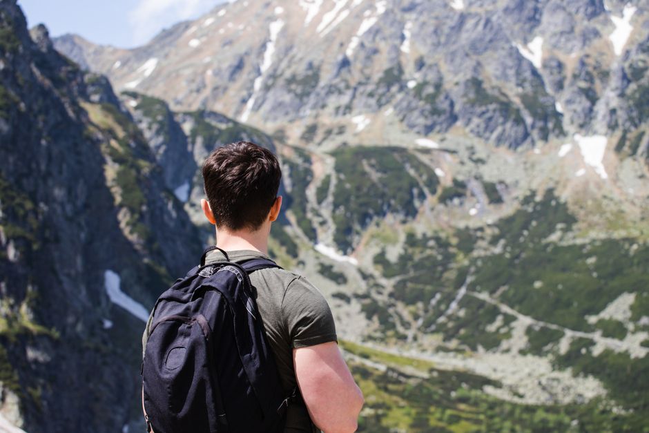 A man with a backpack enjoys a scenic view on a mountain trail in summer.