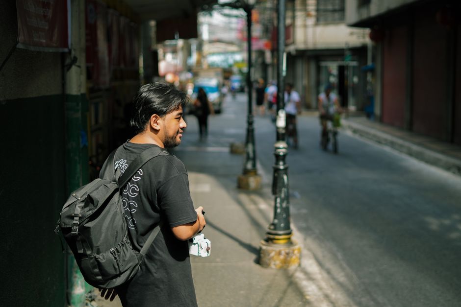 A man with a backpack strolls through the urban city streets in daylight, capturing the essence of city life.