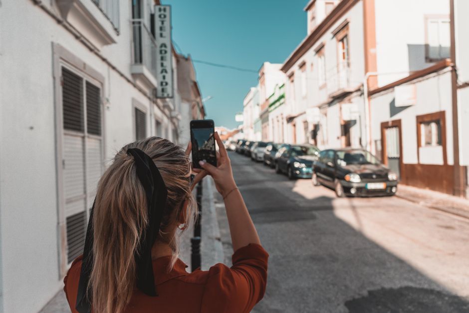 Woman capturing a European street with her smartphone on a sunny day.