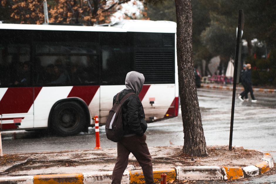 A person in a hoodie walks through city streets as a bus passes by, capturing urban life.