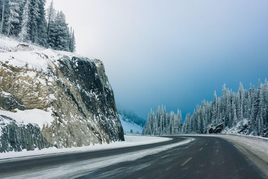 A serene winter landscape featuring a snow-covered road winding through a forested mountain in Field, BC, Canada.