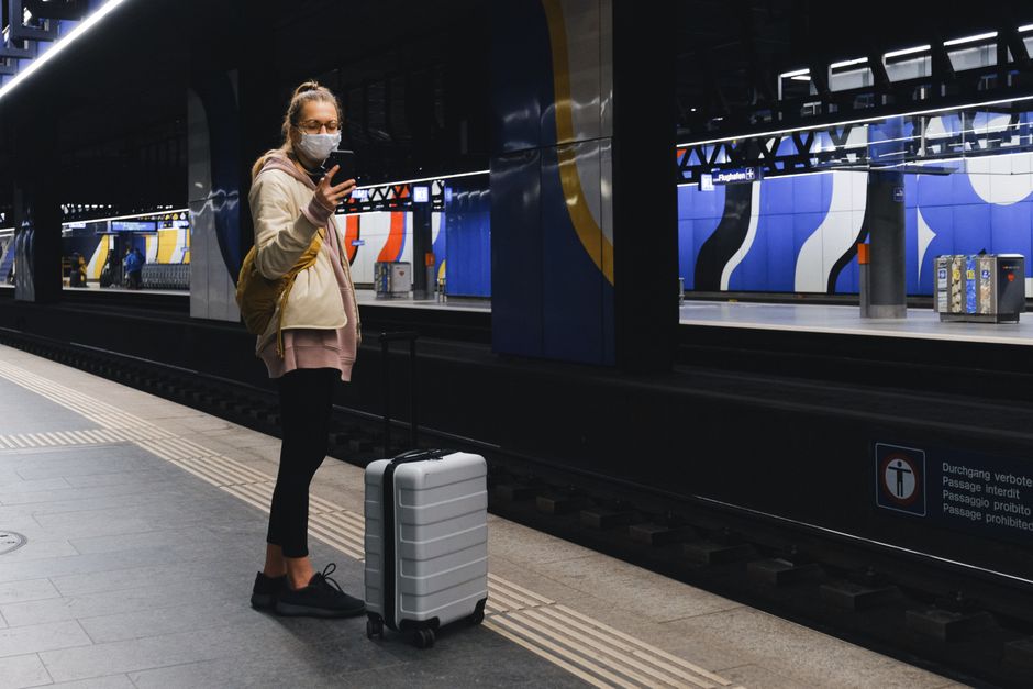 A traveler wearing a mask checks her phone on a subway platform during the pandemic.