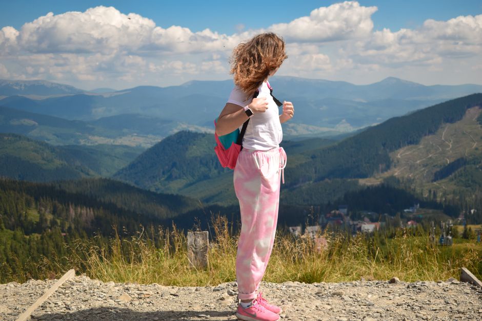 A young woman with a backpack enjoys a scenic mountain view on a sunny day.
