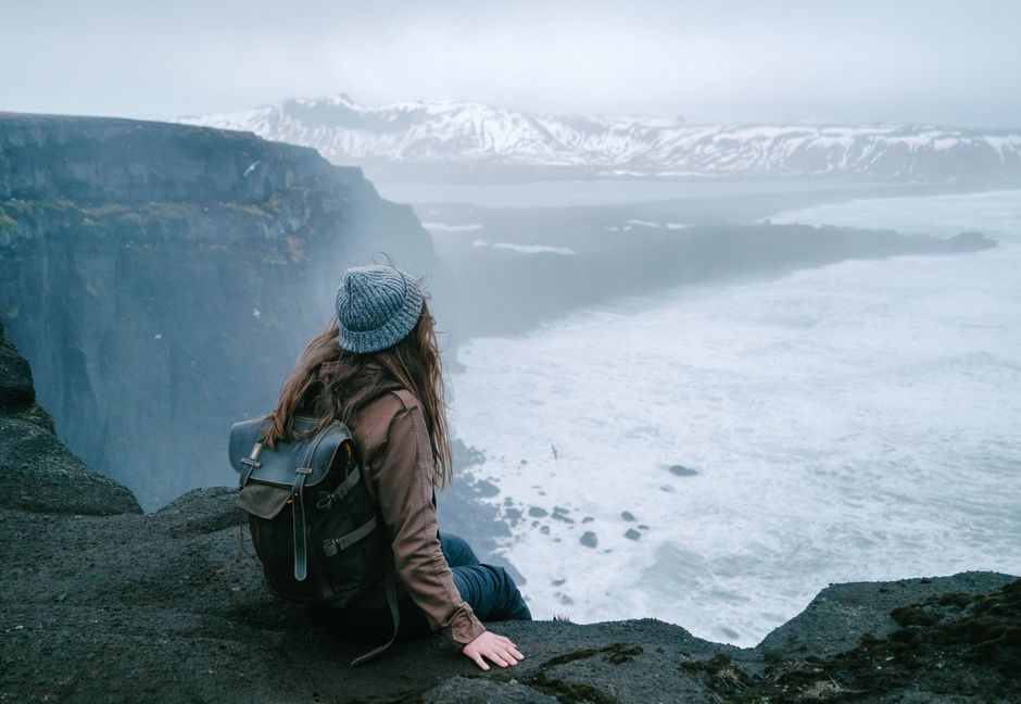 Backpacker enjoys stunning cliffside view over foggy sea and snowy mountains, embodying adventure and travel.