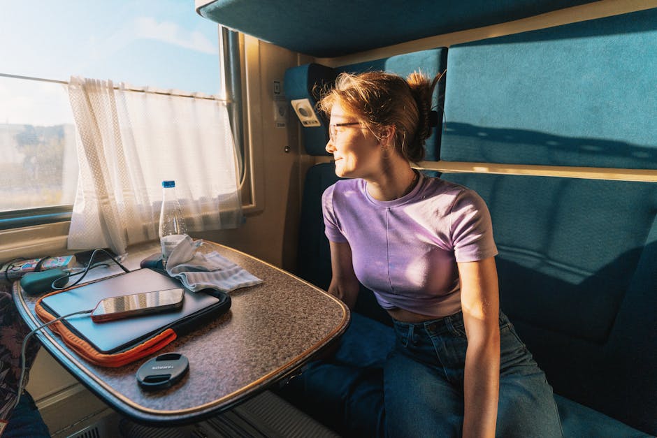 Young woman gazes out train window, enjoying sunny views during daytime travel.