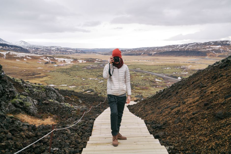 Photographer on a wooden path capturing the vast Icelandic landscape in early spring.