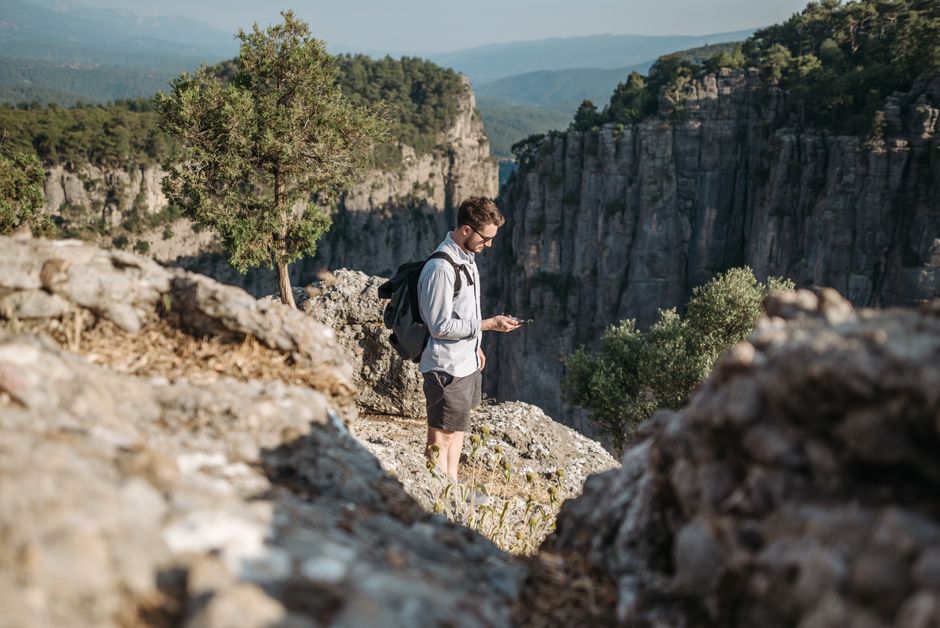 Man exploring rocky cliffside with smartphone. Stunning nature view on a sunny day.