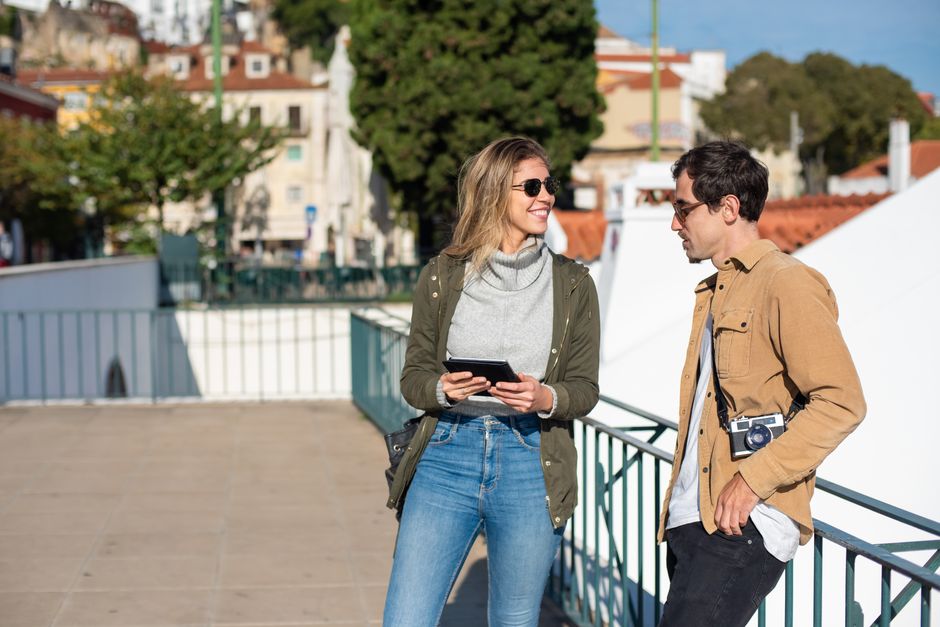 Happy couple exploring city streets with a camera, enjoying sunny day outdoors.