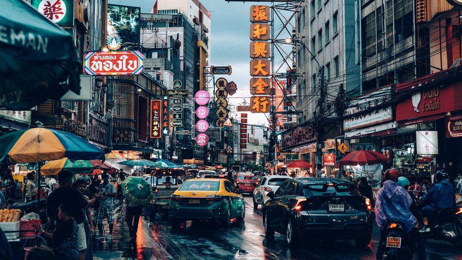 Bustling night market street scene in Bangkok, Thailand with neon signs and traffic.