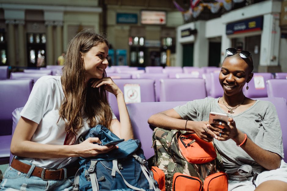 Smiling women with backpacks enjoying time in a waiting area, capturing a travel vibe.
