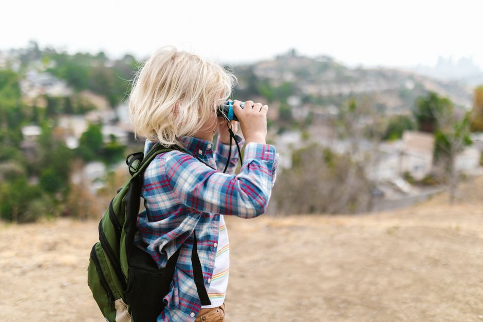 A child with binoculars and a backpack exploring the outdoors on a sunny day.