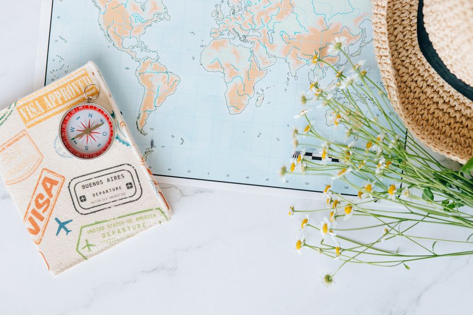 Flat lay of world map, compass, passport, and chamomile flowers, perfect for travel enthusiasts.