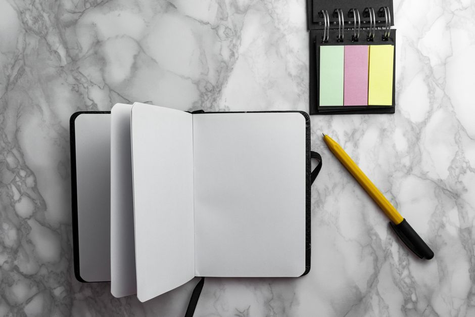 Open notebook with a pen and colorful sticky notes on a marble background. Perfect for writing projects and office setups.