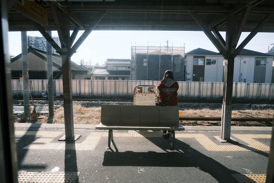 A teenager waits alone on a sunny day at a Toyota railway station platform.
