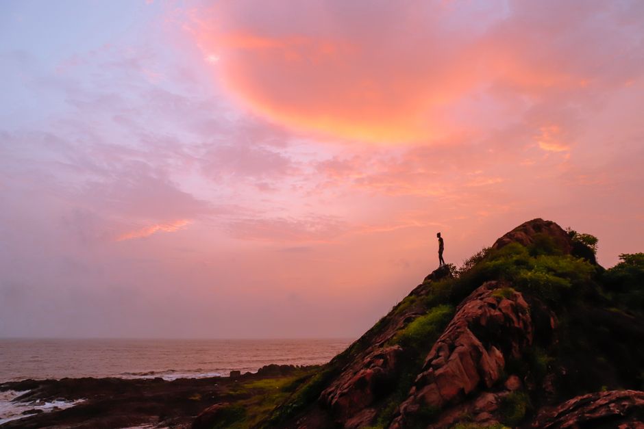 A lone figure stands on a coastal cliff during a vibrant sunset, capturing the essence of adventure and nature.
