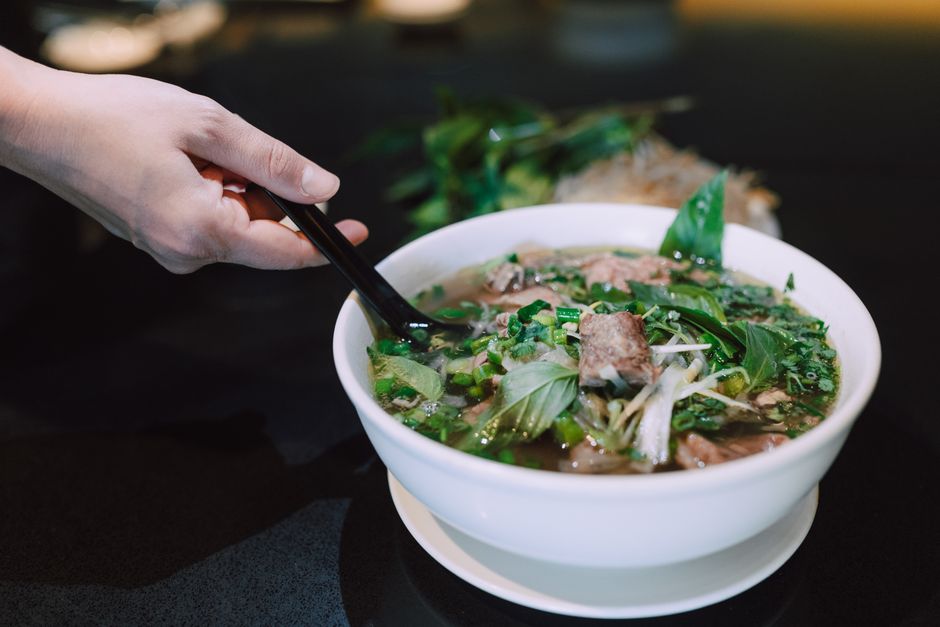 Close-up of a hand holding chopsticks over a bowl of flavorful Vietnamese pho.