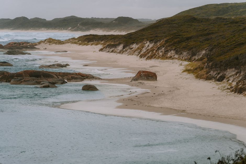 Peaceful view of Yallingup Beach with rolling waves, rocky shore, and misty hills in Western Australia.