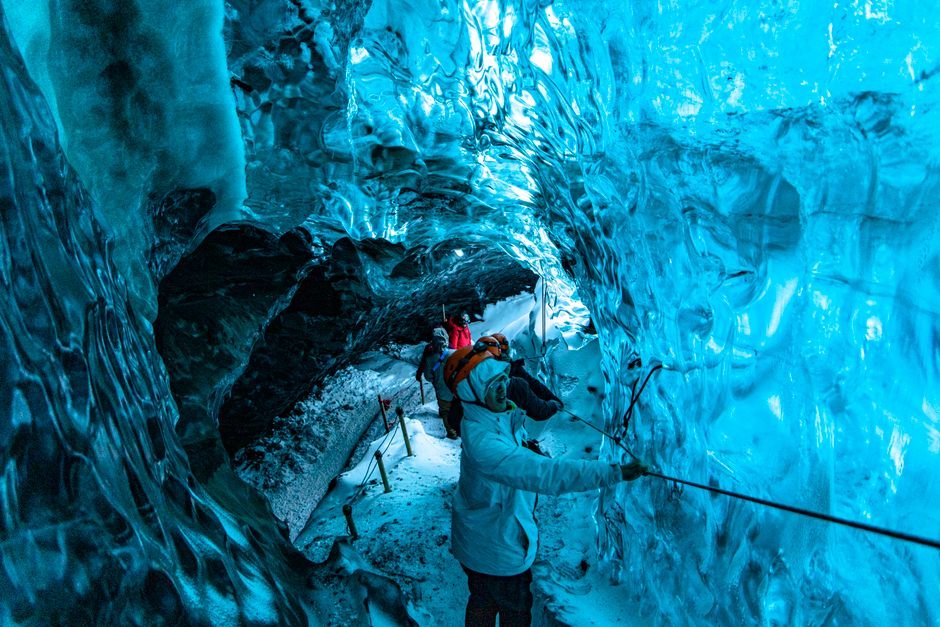 Group exploring a stunning blue ice cave, showcasing glacial textures and colors.